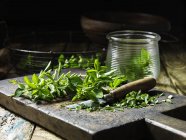 Marjoram, whole and chopped, some in glass jar, vintage knife, rustic wooden chopping board — Stock Photo
