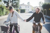 Молода пара їздить на велосипеді, тримаючись за руки — стокове фото