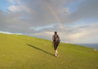 Caminhadas femininas jovens na colina em direção ao arco-íris, visão traseira — Fotografia de Stock
