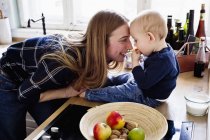 Mulher brincando com o bebê filho no balcão da cozinha — Fotografia de Stock
