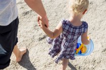 Отец и девочка прогуливаются по пляжу с ведром для игрушек — стоковое фото