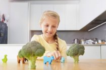 Girl playing with toy animals around broccoli — Stock Photo