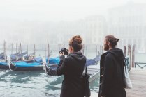 Пара фотографирующих гондолы на туманном канале, Венеция, Италия — стоковое фото