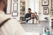 Vista por encima del hombro del barbero preparando al cliente en la peluquería - foto de stock