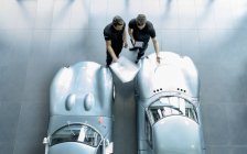 Ingenieros inspeccionando coches de carreras clásicos en la fábrica de coches de carreras, vista aérea - foto de stock