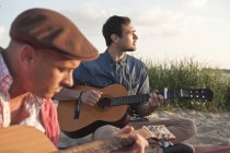 Zwei befreundete Männer spielen Akustikgitarren am Strand, dorset, uk — Stockfoto