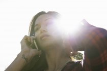 Молода жінка розмовляє по смартфону проти сонячного неба — стокове фото