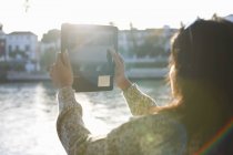 Зрелая женщина-туристка фотографирует реку Гвадалкивир на цифровой планшет, Севилья, Испания — стоковое фото