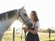 Ritratto di adolescente e il suo cavallo grigio in campo illuminato dal sole — Foto stock
