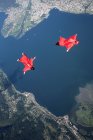 Two wingsuit skydiver pilots team training and flying close together over lake, Locarno, Tessin, Switzerland — Stock Photo