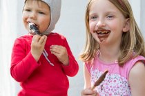Femme tout-petit et soeur messily manger des glaces au chocolat — Photo de stock