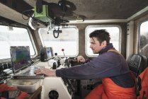 Pescador conduciendo barco de pesca usando ordenador portátil - foto de stock