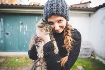 Молодая женщина в вязаной шляпе обнимает кота, смотрит в камеру улыбаясь — стоковое фото