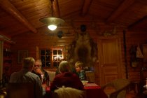 Família de três gerações sentada conversando na mesa de Natal na cabine de madeira à noite — Fotografia de Stock