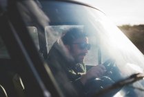 Mann mit Sonnenbrille fährt Auto im Sonnenlicht — Stockfoto