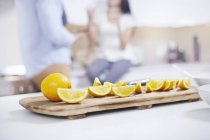 Quartered oranges on kitchen counter with couple on blurred background — Stock Photo