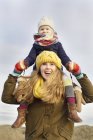 Улыбающаяся средняя взрослая женщина, несущая дочь на плечах на побережье — стоковое фото
