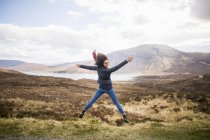 Mujer adulta en las montañas haciendo salto de estrella, Isla de Skye, Hébridas, Escocia - foto de stock