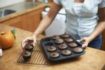 Female hands lifting cup cakes onto cooling rack — Stock Photo