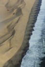 Повітряний вигляд хвиль серфінгу на береговій лінії та піщаних дюнах — стокове фото