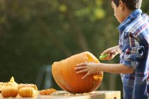 Boy carving pumpkin on table in garden — Stock Photo