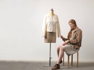 Jovem designer de moda feminina sentada nas fezes fixando blusa no boneco da costureira — Fotografia de Stock