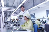 Supervisor que supervisa la estación de control de calidad en la fábrica produciendo placas de circuitos electrónicos flexibles. Planta se encuentra en el sur de China, en Zhuhai, provincia de Guangdong - foto de stock