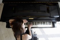 Vista aérea de una mujer madura apoyada en el piano tocando - foto de stock