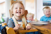 Tres niños pequeños comiendo pastel en la mesa de té - foto de stock
