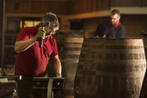 Мужчина-купер использует молоток в кооперативе с бочками виски — стоковое фото