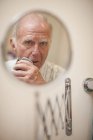 Portrait of senior man in shaving mirror using electric razor — Stock Photo