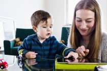 Mujer adulta mediana e hijo bebé usando pantalla táctil en tableta digital en la mesa - foto de stock