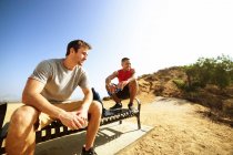 Zwei männliche Freunde, die auf einer Bank auf einer Klippe sitzen und die Aussicht betrachten — Stockfoto