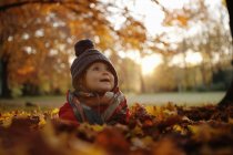 Little girl in hat sitting in autumn leaves — Stock Photo