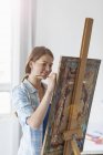 Artista feminina pintura no cavalete dentro de casa — Fotografia de Stock