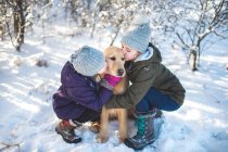Dos chicas jóvenes, abrazando al perro, en un paisaje nevado - foto de stock