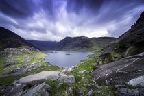 Lac entouré de collines verdoyantes sous un ciel nuageux — Photo de stock