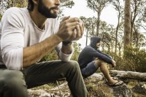 Two men drinking coffee whilst sitting on fallen tree, Deer Park, Cape Town, South Africa — Stock Photo