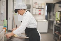 Pâte à rouler femelle boulanger dans la cuisine — Photo de stock