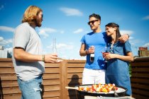 Couple chatting to male friend at rooftop party — Stock Photo