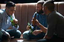 Tres amigos masculinos charlando y bebiendo en el pub tradicional del Reino Unido - foto de stock