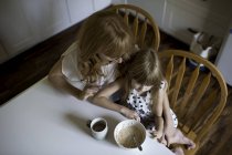 Madre e hija abrazándose en la mesa del desayuno - foto de stock