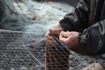 Рыбак чинит сеть на галечном пляже — стоковое фото