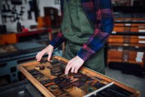 Colheita de jovem artesão olhando através da bandeja de cartas de madeira tipografia em oficina de impressão — Fotografia de Stock