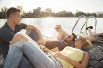 Quattro giovani amici adulti in chat sul molo lungo il fiume — Foto stock
