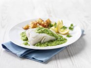 Haddock fish fillet with fried potatoes, minted pea sauce and lemon wedges — Stock Photo