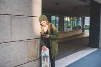 Молодий чоловік міський скейтбордист спирається на стіну читання текстів смартфона — стокове фото