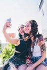 Две молодые женщины на стене делают селфи на смартфоне в городском жилом комплексе — стоковое фото
