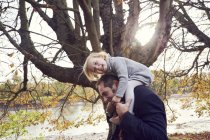 Father carrying daughter on shoulders in autumn park — Stock Photo