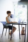 Средняя взрослая мать печатает на ноутбуке с дочкой малыша под столом — стоковое фото